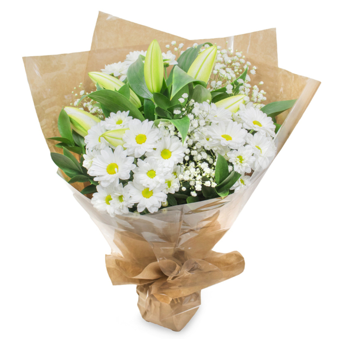 The image shows a serene white and green bouquet standing upright against a bright white backdrop, its clean lines and soft textures reminiscent of a thoughtfully arranged tribute at a quiet gathering in Tulse Hill. The bouquet is dominated by clusters of daisy-like white chrysanthemums, their petals neat and plentiful, radiating from round, lime-tinged centres that glow gently rather than shout for attention. These daisies are arranged densely, giving the bouquet a rounded, pillowy silhouette that feels both generous and gentle to the eye. Rising above and among them are several elongated lily buds, still firmly closed, their outer petals shaded in fresh green that melts into off-white at the edges. They stretch lightly upward, adding height and an elegant sense of possibility, as if marking the beginning of a new chapter after a difficult farewell. Fine stems of white gypsophila thread through the design, each tiny flower a pinpoint of light that softens the outlines and adds a dreamy, veil-like texture. Around the perimeter, substantial dark green leaves provide structure and contrast, their glossy surfaces reflecting the soft, even lighting that fills the scene. The stems at the base are pulled together tightly and wrapped in rustic brown kraft paper, creased and folded to form a protective collar that looks as natural as the trees lining nearby Brockwell Park. Over this sits a sheath of clear cellophane, barely visible except for a few gentle reflections, ensuring the bouquet is ready for careful delivery. Everything about this arrangement suggests purity, remembrance, and calm support, suitable for sympathy messages and memorial tributes across Tulse Hill and the surrounding neighbourhoods.