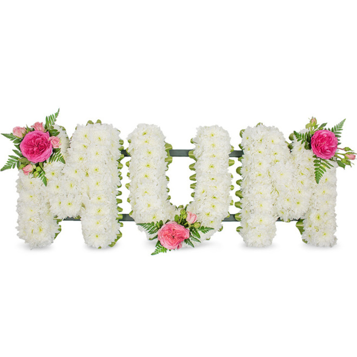 The image shows a tender "MUM" funeral tribute, arranged in large, bold capital letters that seem to rest gently against a seamless white backdrop, allowing every petal and detail to stand out clearly. Each letter is densely filled with pristine white spray chrysanthemums, their compact heads placed so close together they form a plush, uniform surface resembling a soft quilt of blossoms. The texture is slightly domed and three-dimensional, catching the light in subtle highlights and shadows that suggest depth and immaculate freshness. Around the base of the letters, a dark green frame and ribbon edging is just visible, providing structure much like the sturdy frames used in professional funeral workrooms around Tulse Hill and neighbouring Brixton. This green outline not only supports the blooms but also gives a refined border that contrasts beautifully with the snowy flowers. To soften the formality of the white, three artfully placed clusters of pink flowers and foliage bring warmth and personality. On the top left of the first "M" sits a lush fuchsia garden rose, fully opened, cradled by smaller pink spray roses and delicate green fern fronds. A similar cluster rests in the lower centre of the "U", and the final matching accent graces the top right of the second "M", creating a gentle visual arc from left to right. The combination of white chrysanthemums, symbolising respect and remembrance, and pink roses, associated with gratitude and motherly love, makes this design a classic choice for funerals, memorials, or graveside tributes. Crafted with the care you would expect from a seasoned Tulse Hill florist, the tribute conveys a message of enduring love for a cherished mum, quietly echoing the comfort and closeness of family gatherings in the local community.